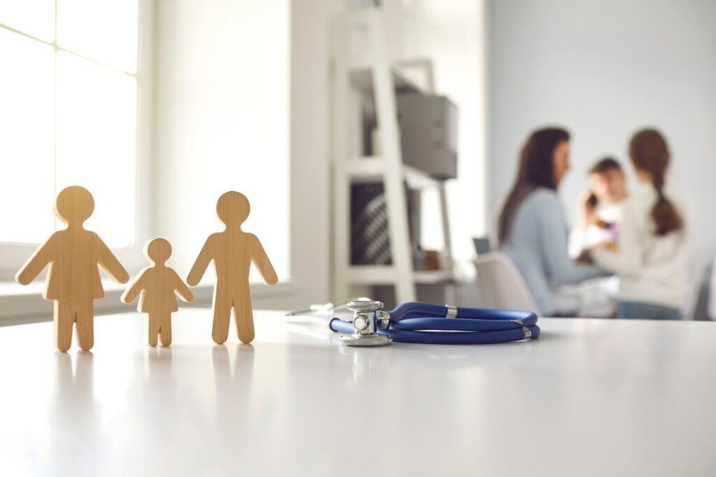 Stethoscope and small wooden family member figures on doctor's table at the hospital